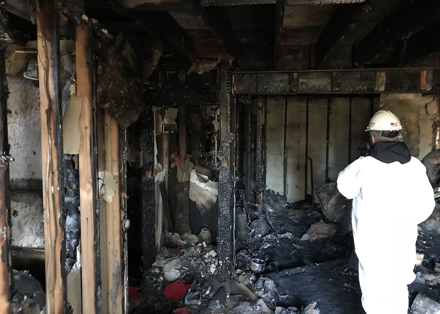 Restoration technician in protective gear inspecting a fire-damaged room